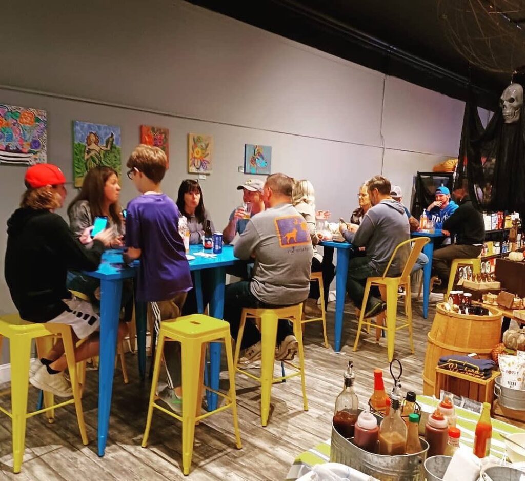 People eating and drinking at tall blue metal tables with yellow metal stools