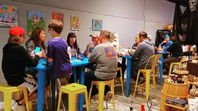 People eating and drinking at tall blue metal tables with yellow metal stools