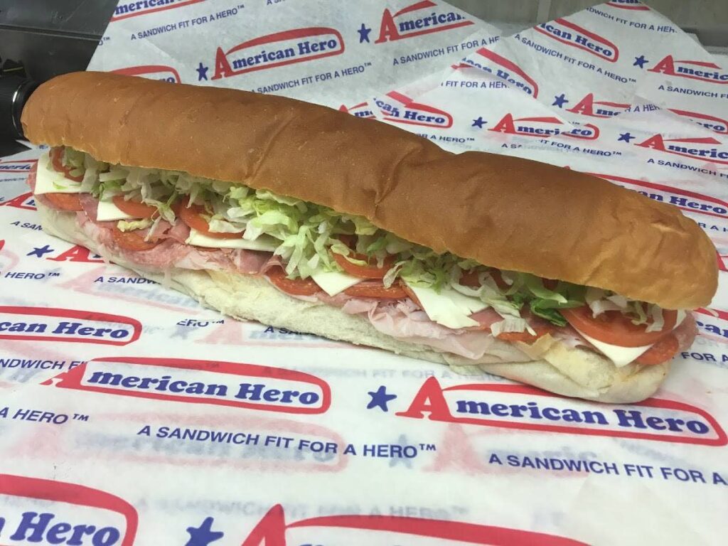 A sub sandwich with lettuce, tomato, cheese, and meat on an American Hero wrapper