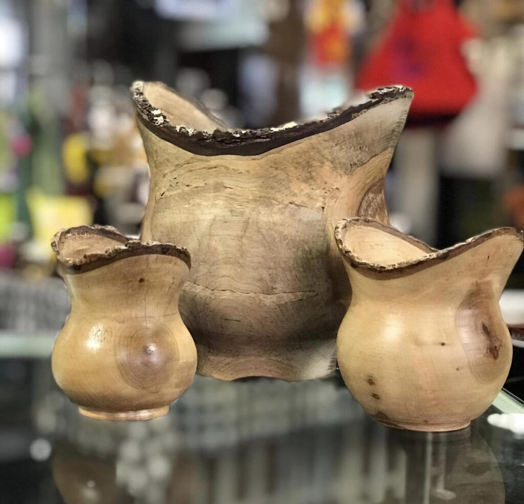 Three wooden vases with curved rims sit on a glass display case