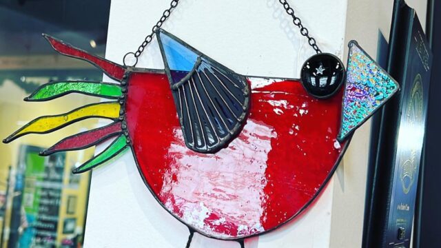 A stained glass bird designed in a modern style hangs from a nail on a white pillar