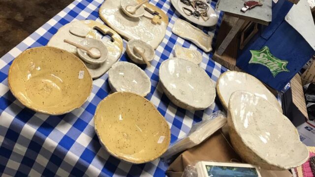 Pottery dishes sit on display on a table covered with a blue checked tablecloth at an artisan emporium