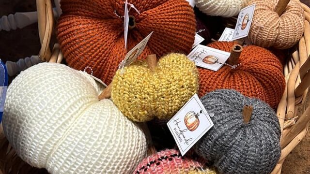 Knitted pumpkins in fall colors sit in a wooden basket