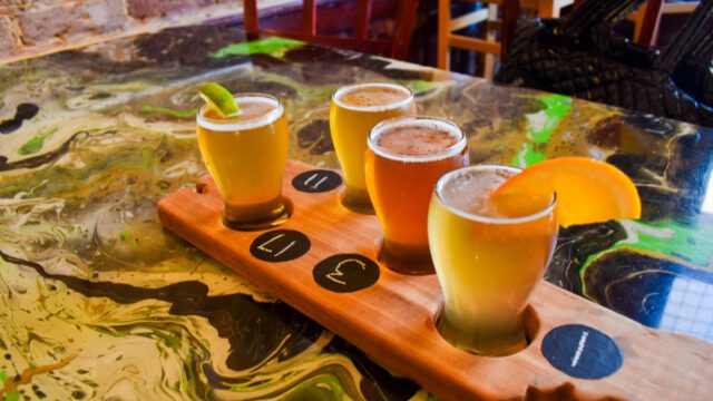 Four glasses of beer in a wooden platter on top of a table