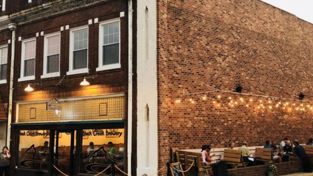 A red brick brewery building with booths on the side of the building and tables visible inside the brewery