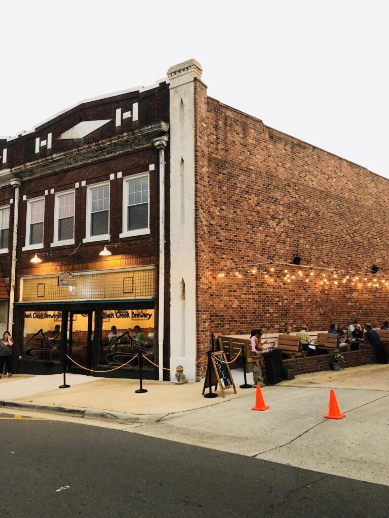 A red brick brewery building with booths on the side of the building and tables visible inside the brewery