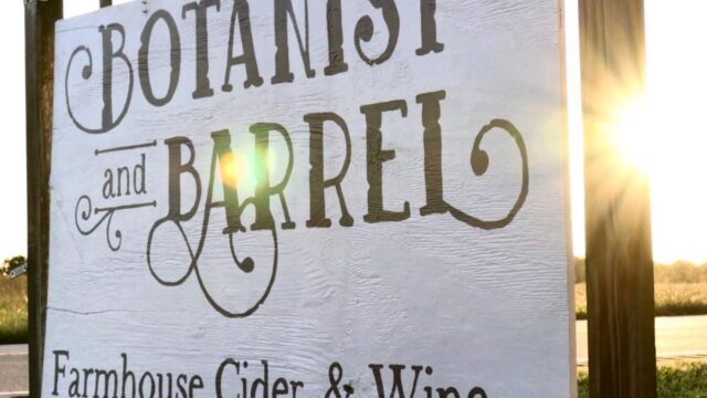 A white painted wooden sign reading Botanist and Barrel, Farmhouse Cider & Wine