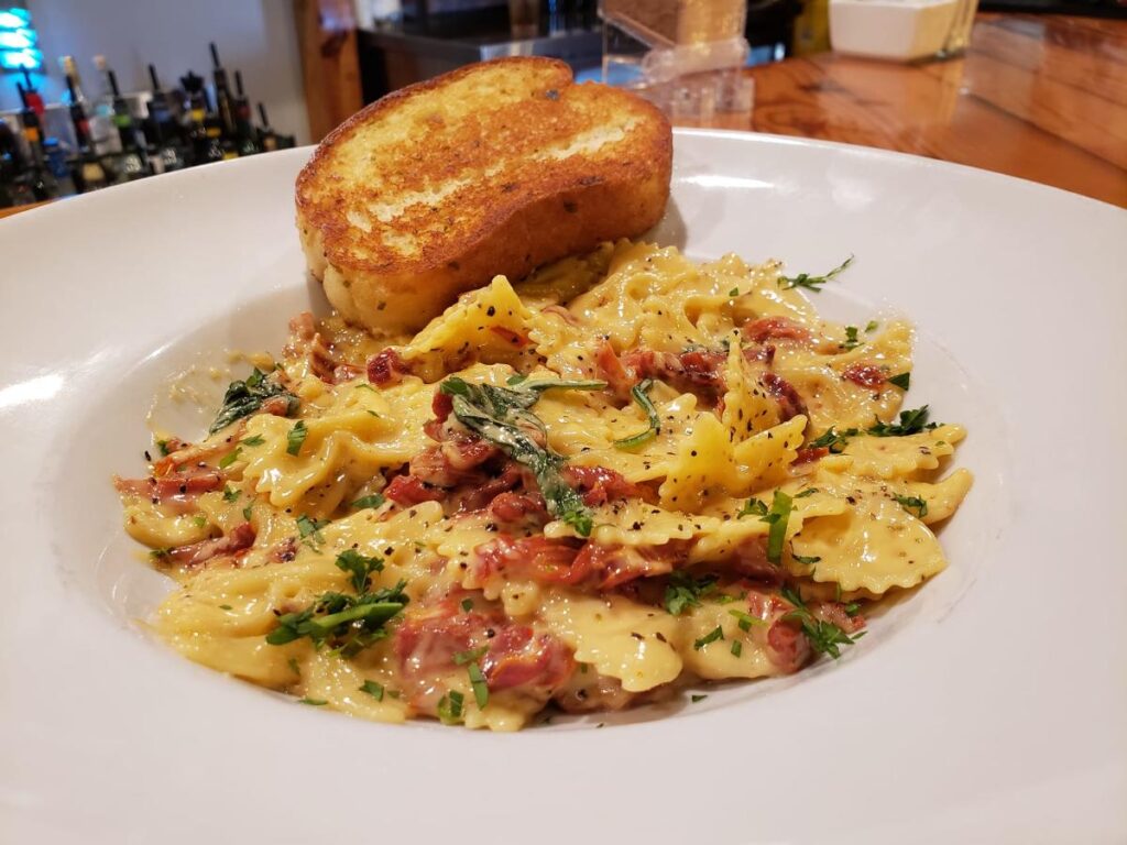 A white dish of pasta with a slide of garlic toast