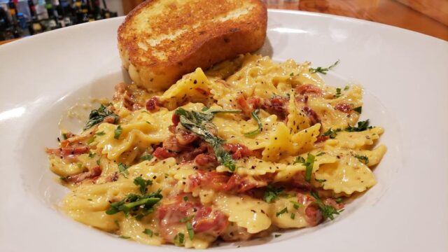 A white dish of pasta with a slide of garlic toast