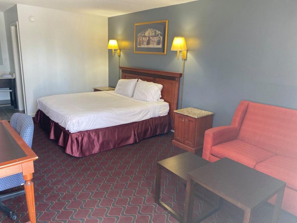 A hotel room with a queen size bed, a red couch, a wooden coffee table, and a desk