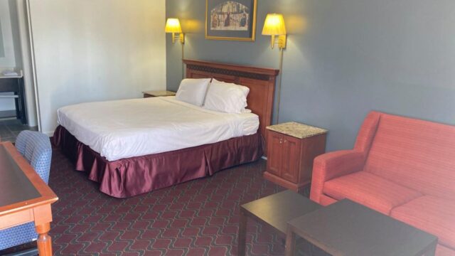 A hotel room with a queen size bed, a red couch, a wooden coffee table, and a desk