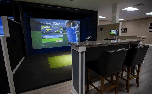 A bar counter with two black chairs facing a TV screen