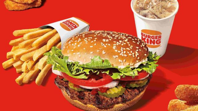 A Burger King Whopper, French fries, chicken nuggets and a soda on a red background
