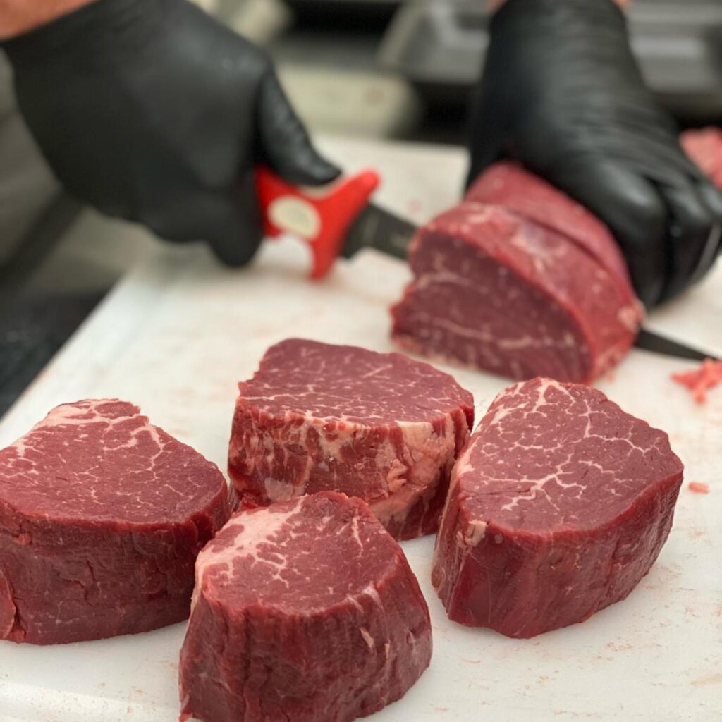 A butcher wearing black plastic gloves slices raw meat on a counter