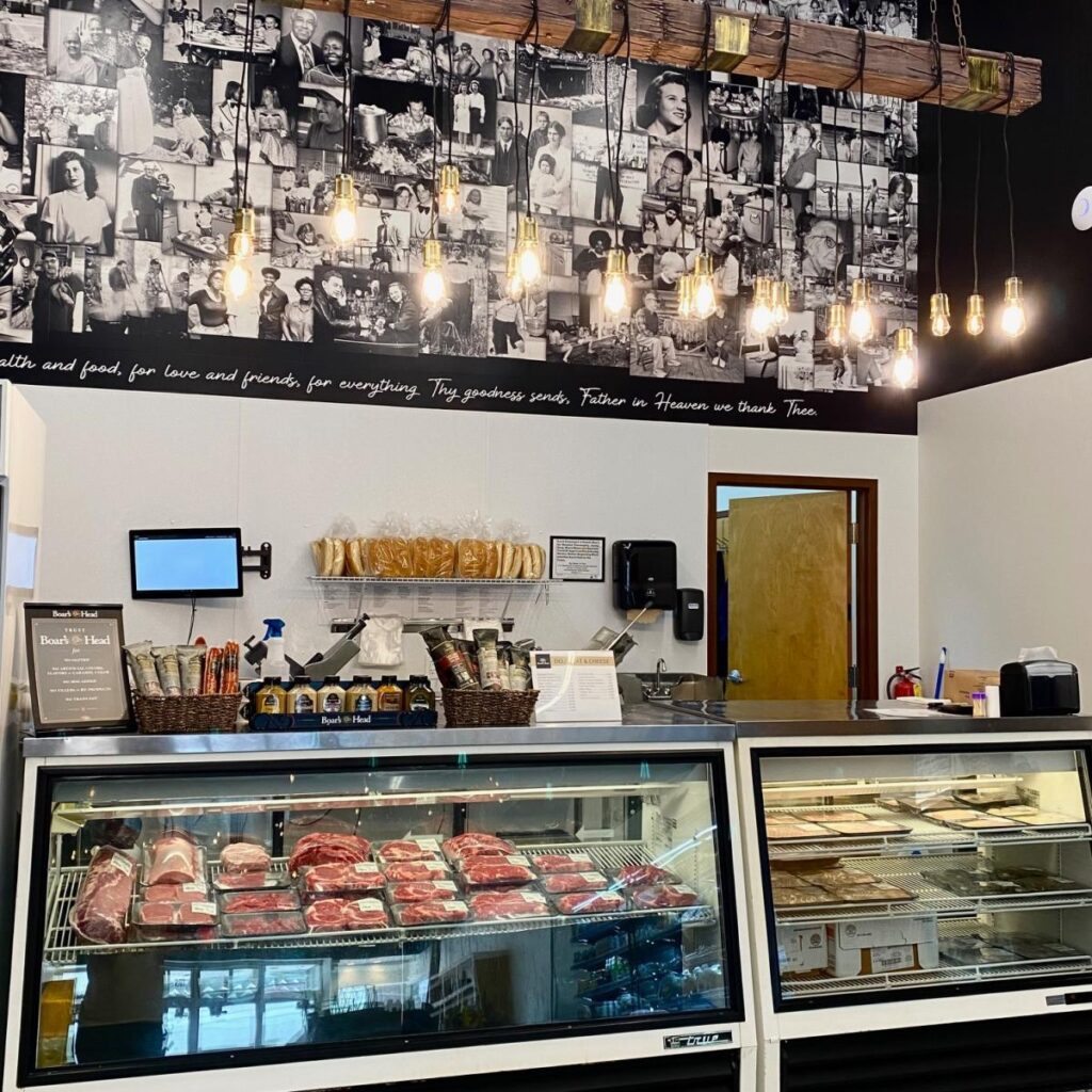 Cuts of meat displayed in a glass case in a butcher shop, with a wall of black and white photographs displayed on the wall behind