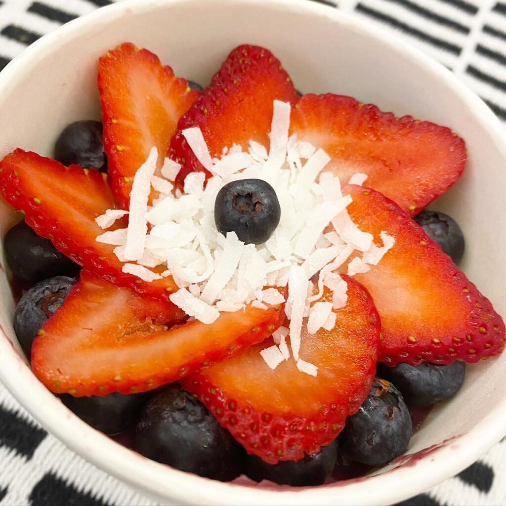 Sliced strawberries fanned out in a flower shape on top of blueberries with coconut flakes and a blueberry on top