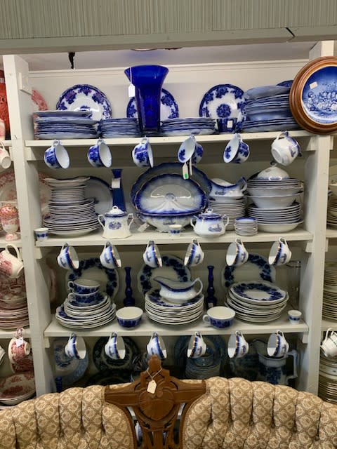 White shelves display white and blue plates, teacups, teapots, and serving dishes