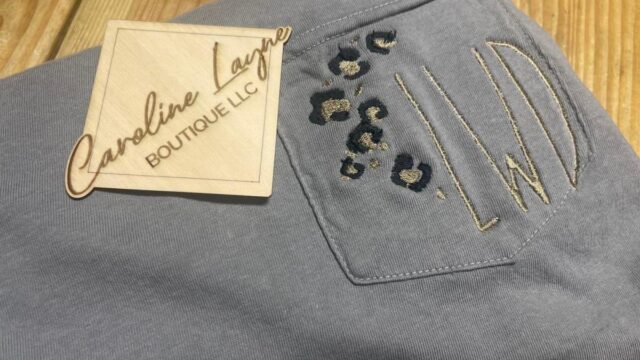 A gray knit piece of clothing with leopard print embroidery and a tag reading Caroline Layne Boutique LLC