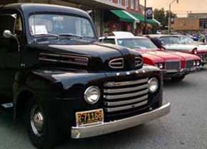 A black classic truck with other classic cars parked behind