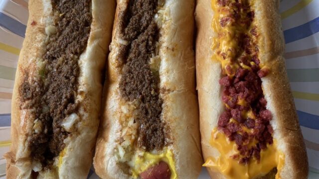 Three hot dogs with toppings served on a colorful paper plate