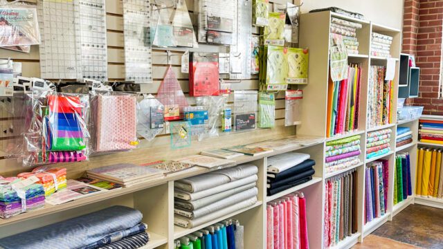 Shelves at a craft store with bolts of fabric and craft notions