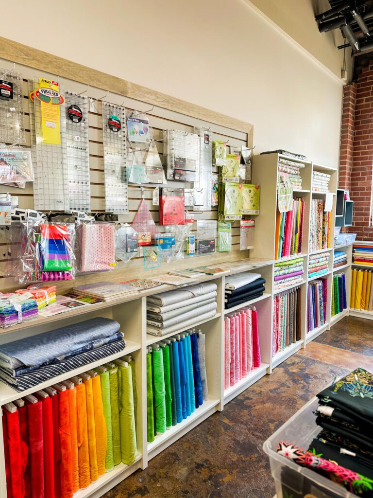 Shelves at a craft store with bolts of fabric and craft notions