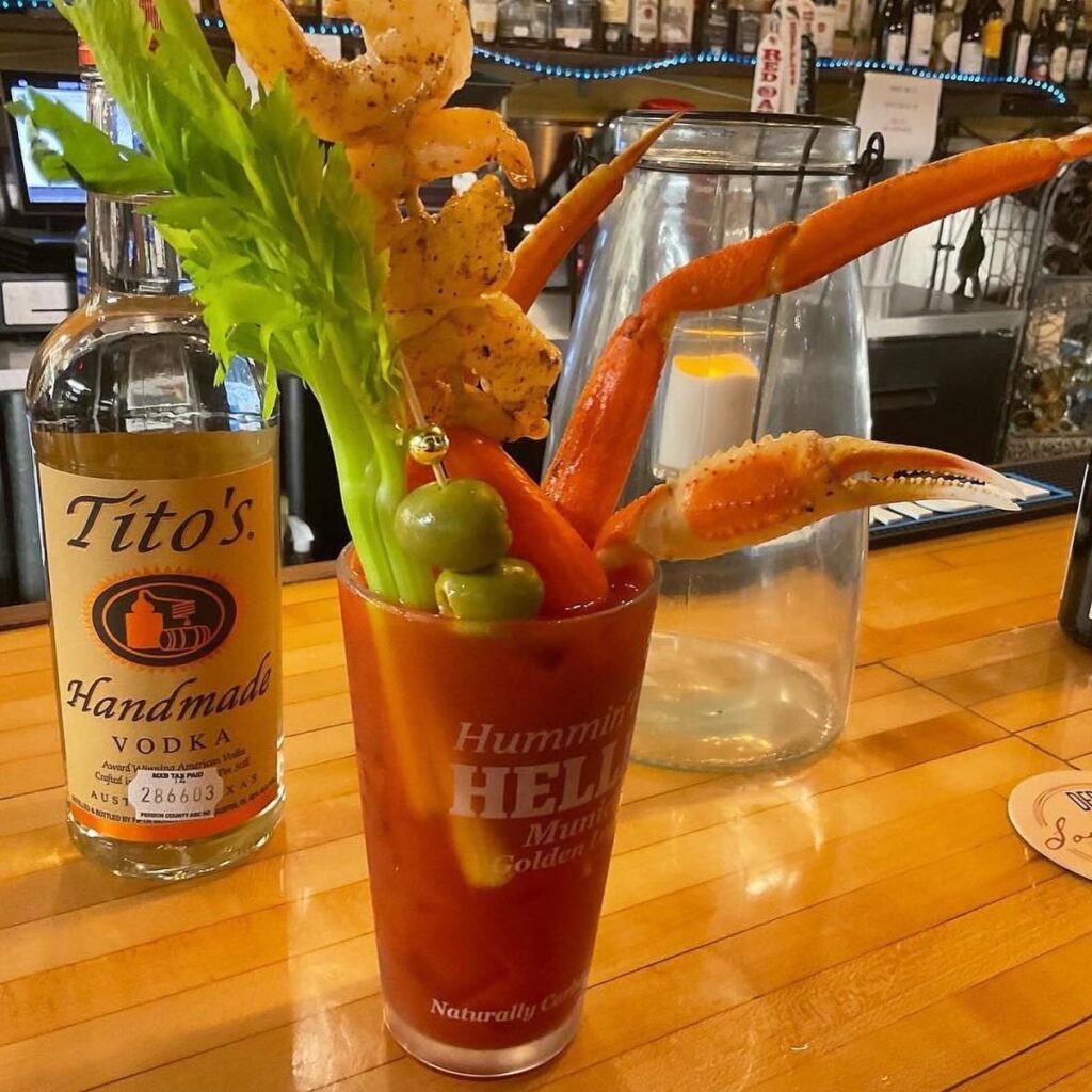 A Bloody Mary drink topped with a stalk of celery, green olives, skewered shrimp and a crab leg