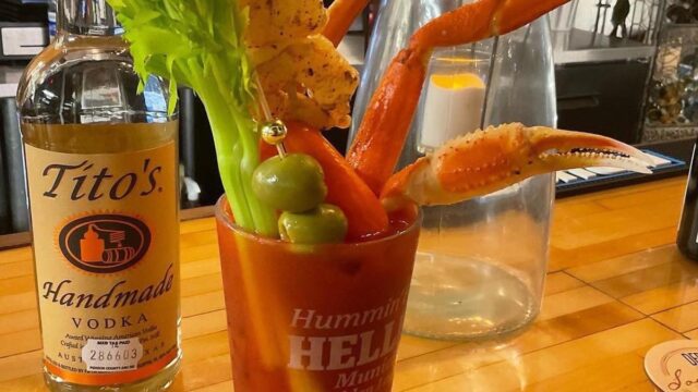 A Bloody Mary drink topped with a stalk of celery, green olives, skewered shrimp and a crab leg