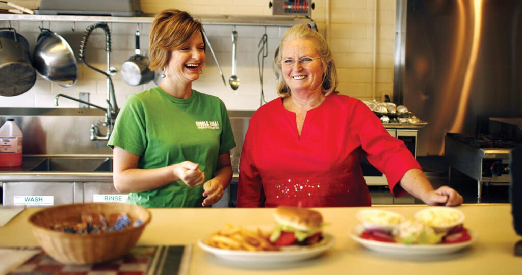 Two women smile behind a restaurant counter