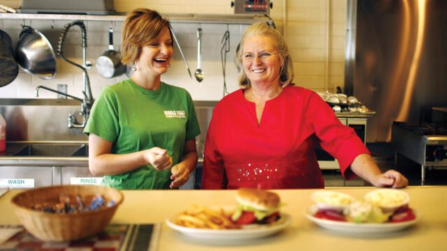 Two women smile behind a restaurant counter