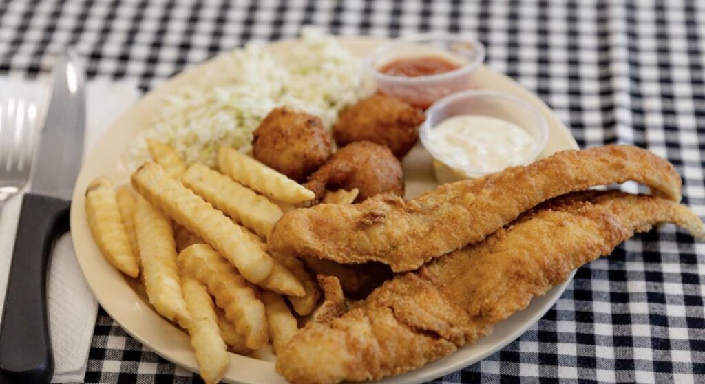 A white plate with fried fish, French fires and coleslaw on a black and white checked tablecloth