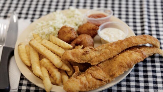 A white plate with fried fish, French fires and coleslaw on a black and white checked tablecloth