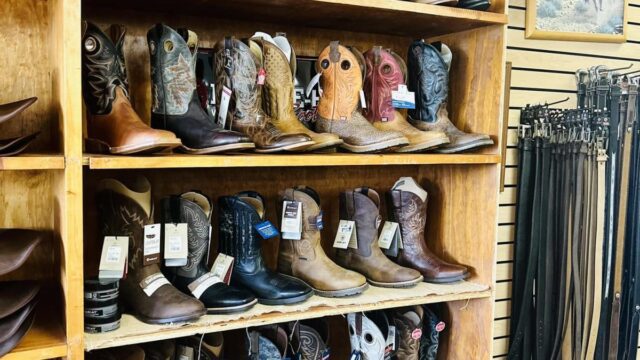 A wooden shelf with cowboy boots on display inside a store
