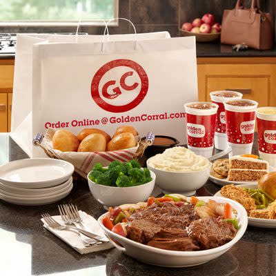 White dishes of beef, broccoli, mashed potatoes, bread rolls, and a slice of carrot cake plus empty plates, cutlery and beverages displayed in front of a Golden Corral to-go bag