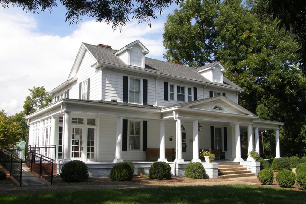 A white two-story house with a large front porch and a ramp on the left side
