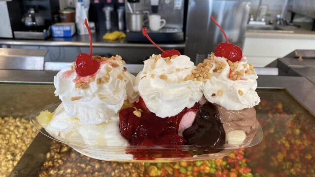 A banana split topped with whipped cream and maraschino cherries on top of a restaurant counter