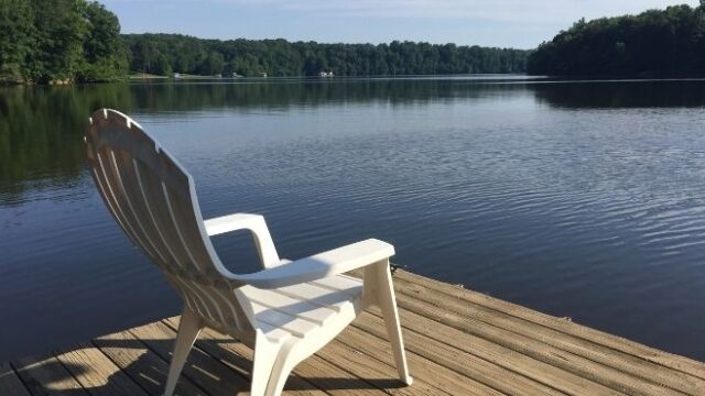 A white Adirondack chair sits on a dock facing the water