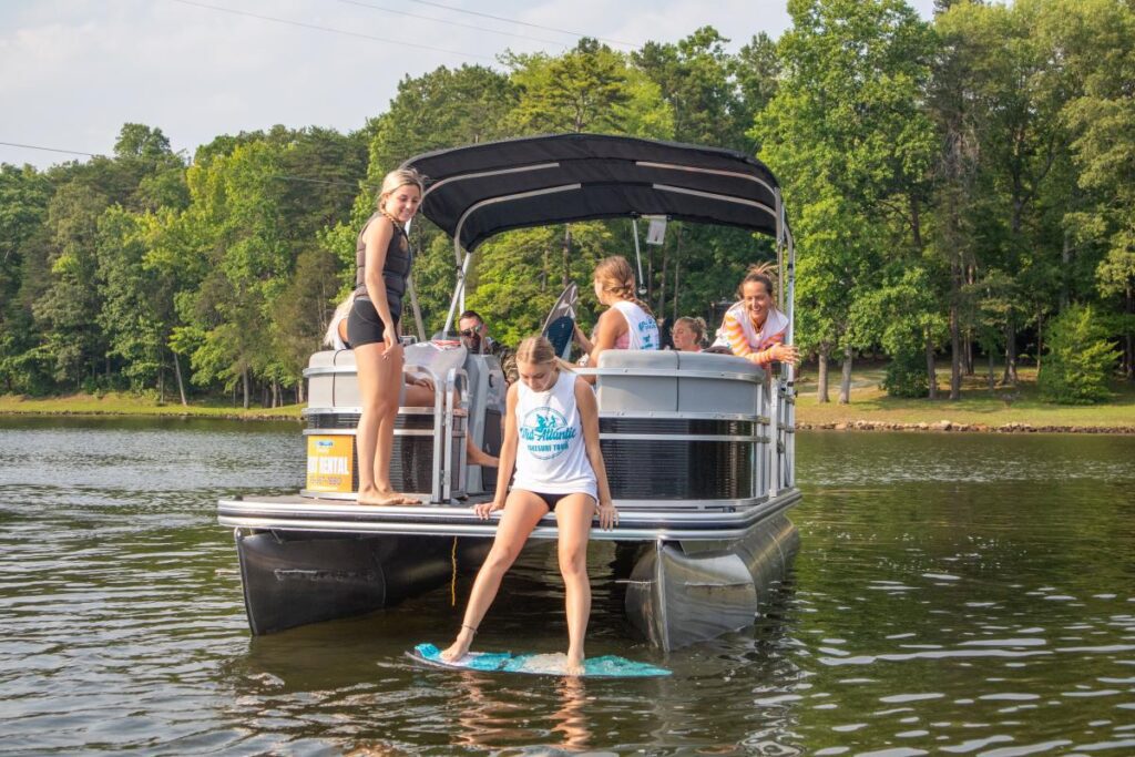 A teenage girl tests a waterboard from the back of a boat filled with teenage girls