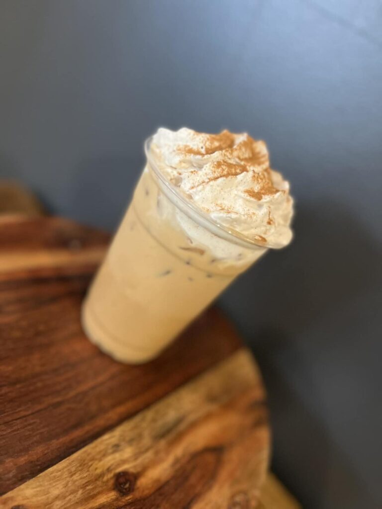 An iced coffee topped with whipped cream in a plastic cup sits on a wooden table