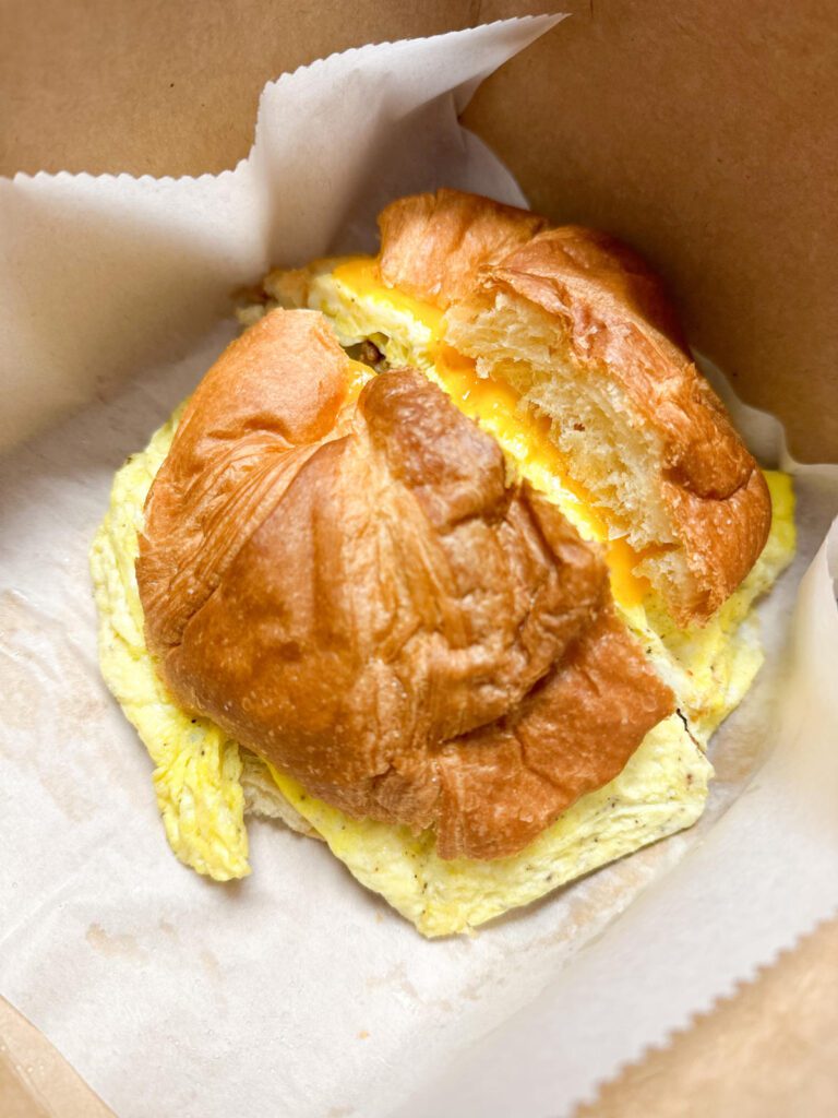 A biscuit sliced in half sits in a brown cardboard to-go container