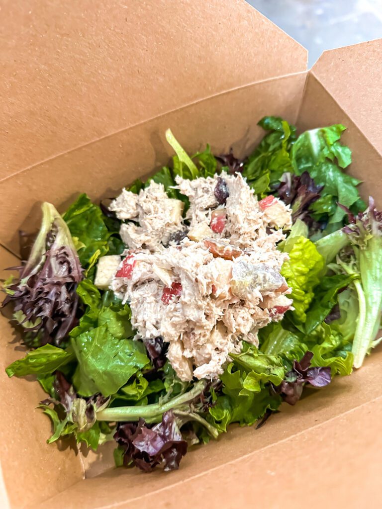 A brown cardboard to-go container filled with tuna salad on a bed of lettuce