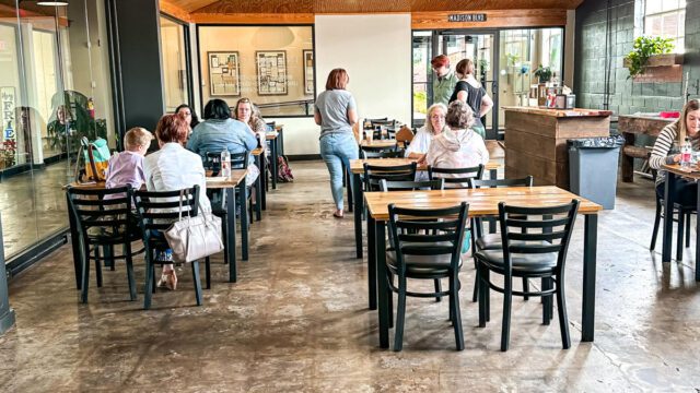 Diners sit in a restaurant with wooden tables and black chairs