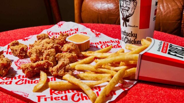 Chicken fingers and French fries spilling out of the fry container onto a white Kentucky Fried Chicken wrapper on a red table