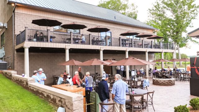 Small groups of people chat in an outdoor courtyard surround by small tables and brown umbrellas