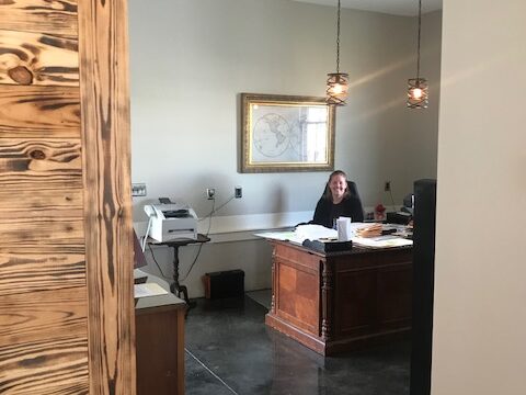 A person smiles and sits at a wooden desk in a law office