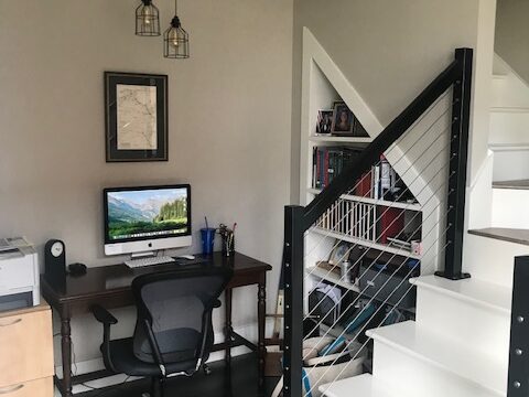 A small wooden desk with a computer next to a white staircase