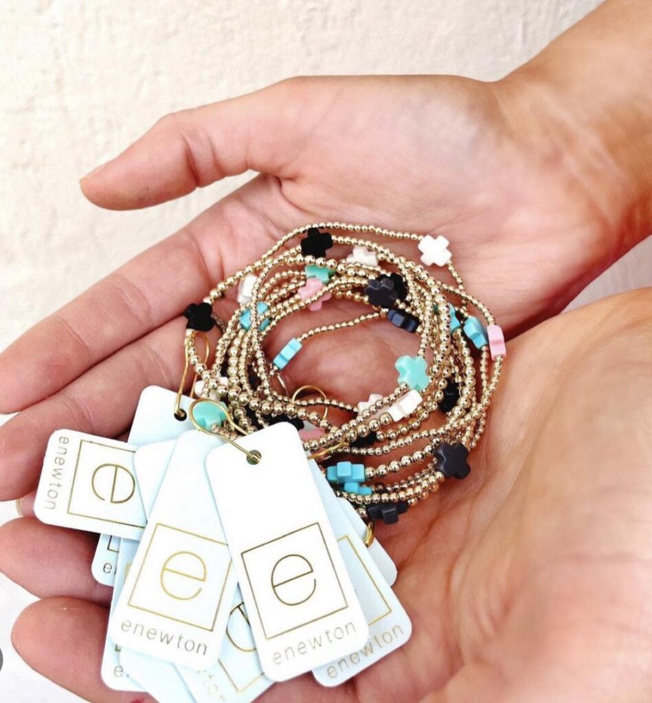 A woman holds a number of gold beaded bracelets with pink, green, white, and black charms