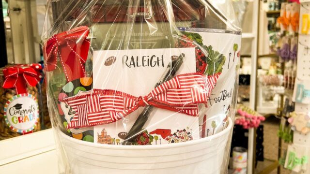 A gift bag in a white plastic bucket wrapped in cellophane and topped with a red bow