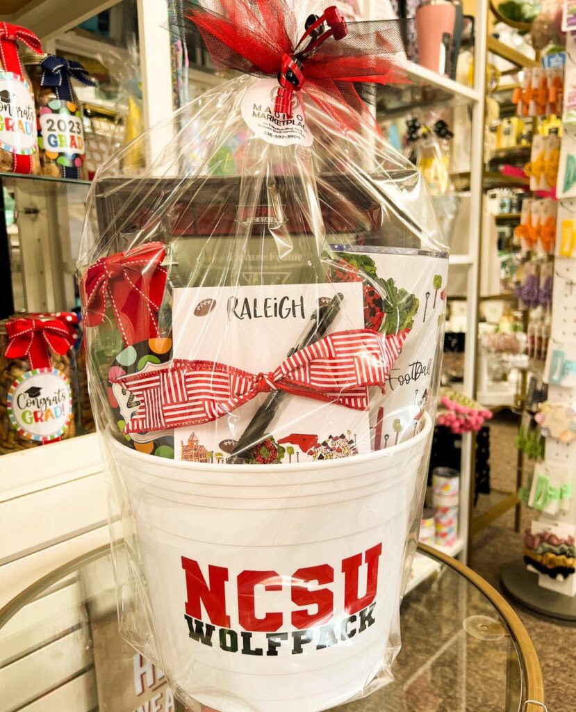 A gift bag in a white plastic bucket wrapped in cellophane and topped with a red bow