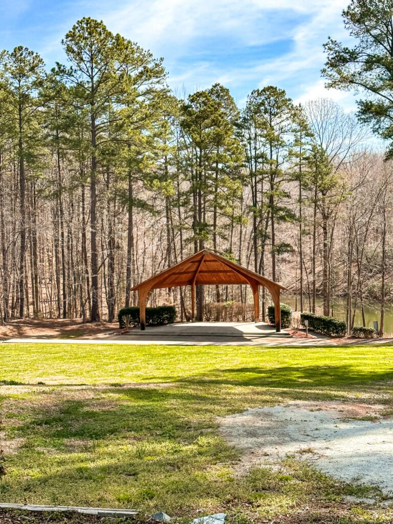 A wooden gazebo surrounded by green grass and tall trees